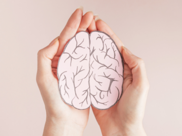 foto de mulher segurando um pedaço de cartolina em formato de cérebro ilustra artigo sobre relação entre saúde mental e ocular.